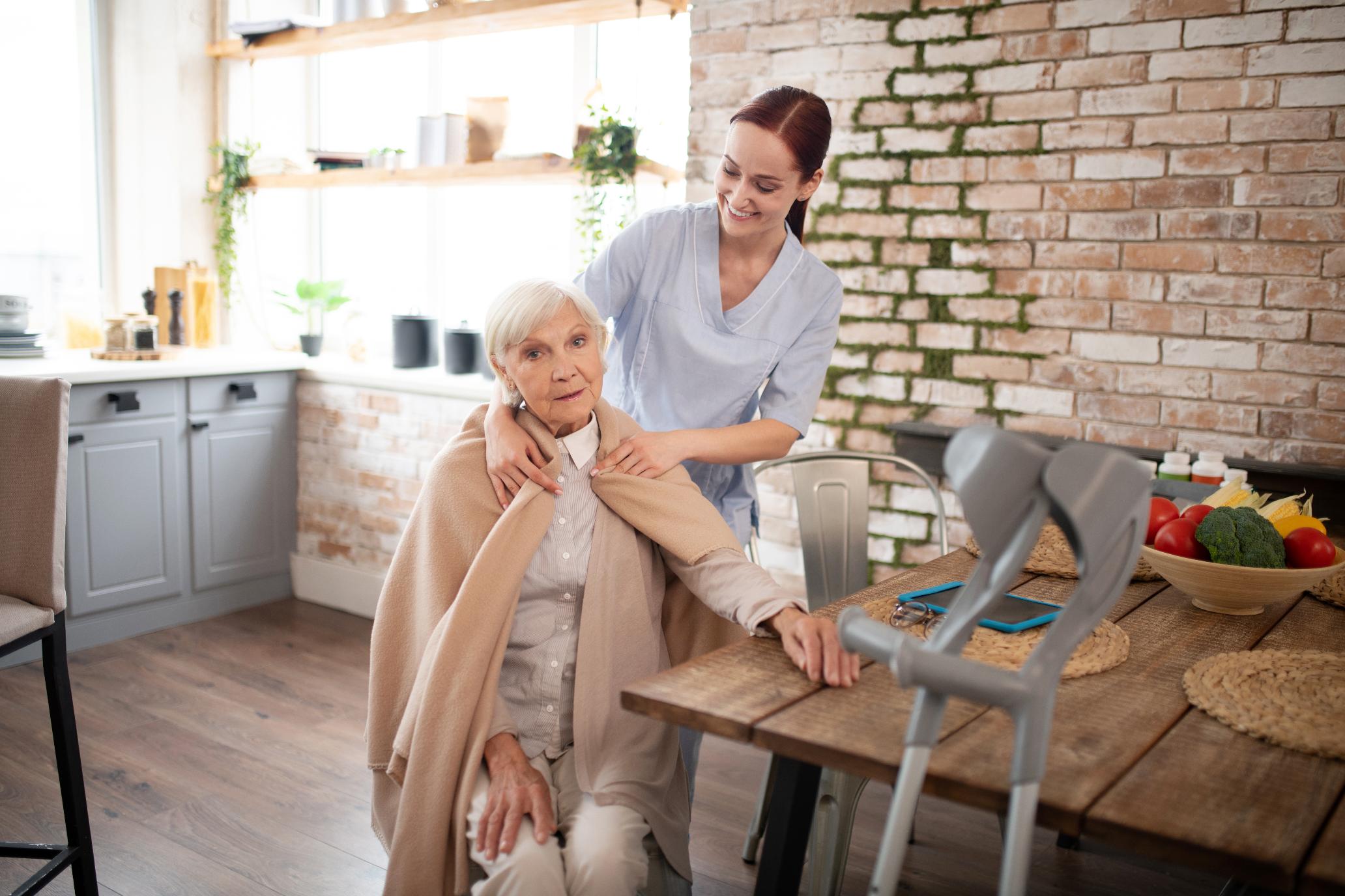 fursorgliche-krankenschwester-die-plaid-auf-schultern-der-gealterten-frau-setzt